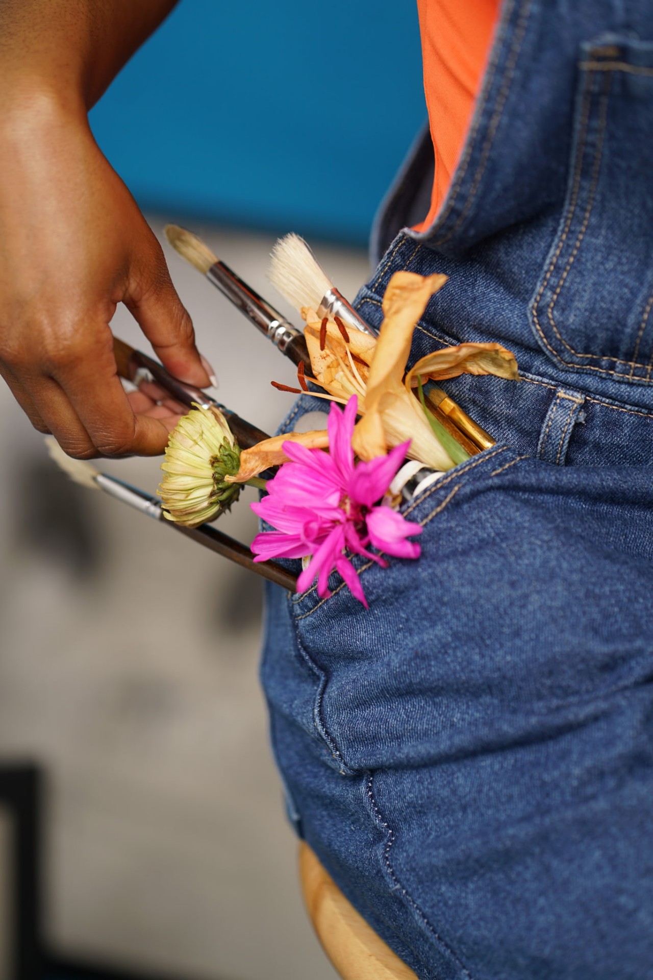 Paintbrushes and fresh flowers tucked into the pocket of denim overalls