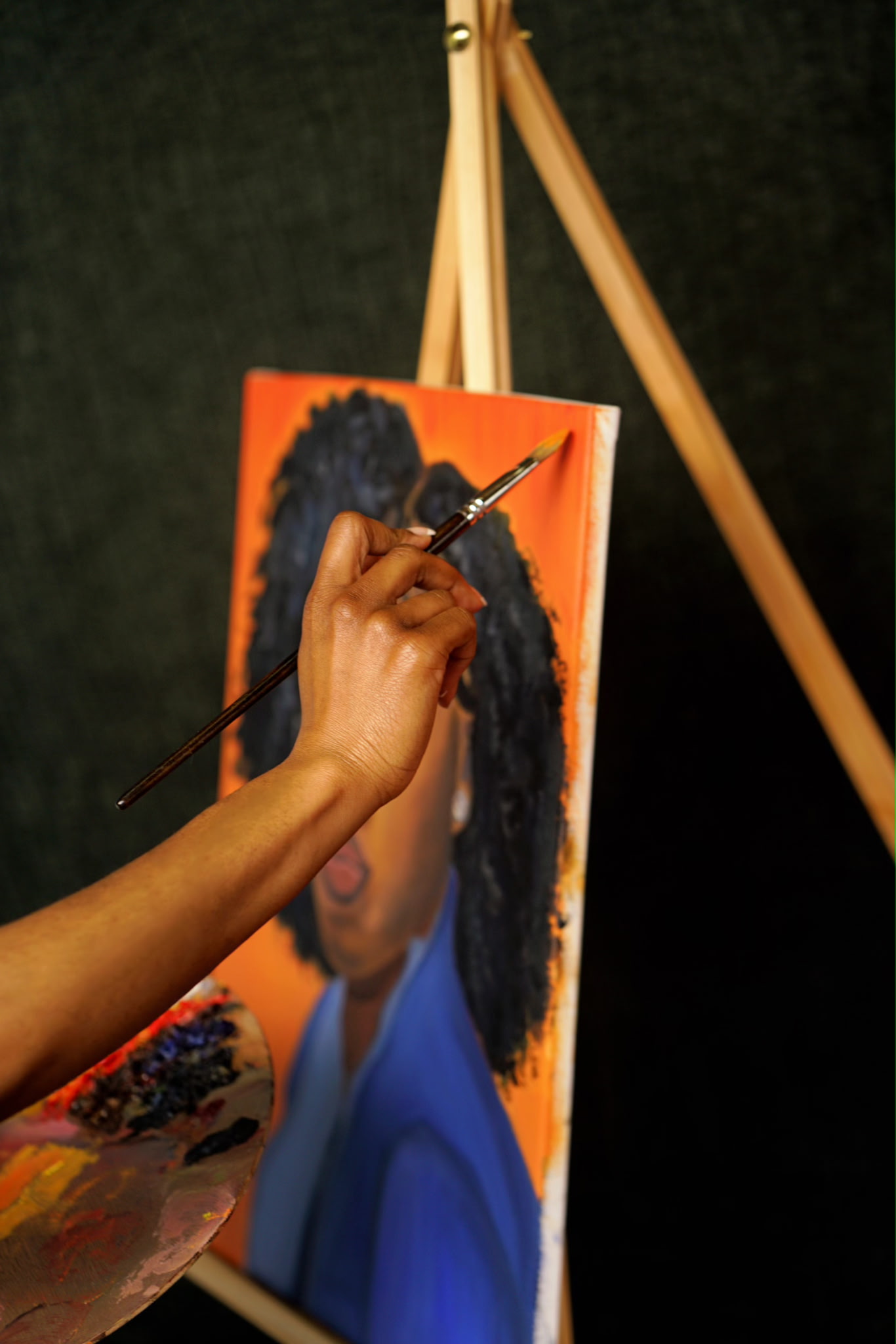 Detail of Carlynn's hand painting curls onto an orange portrait canvas
